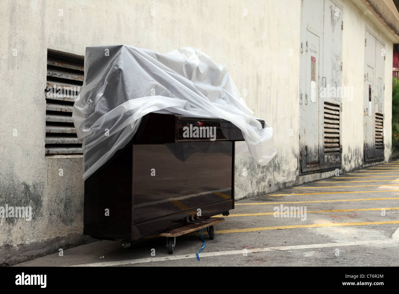 C'est une photo d'un piano sous une couche de plastique ou de couvrir le long d'un mur sale quelque part à Hong Kong. Dans une zone industrielle. Music Banque D'Images