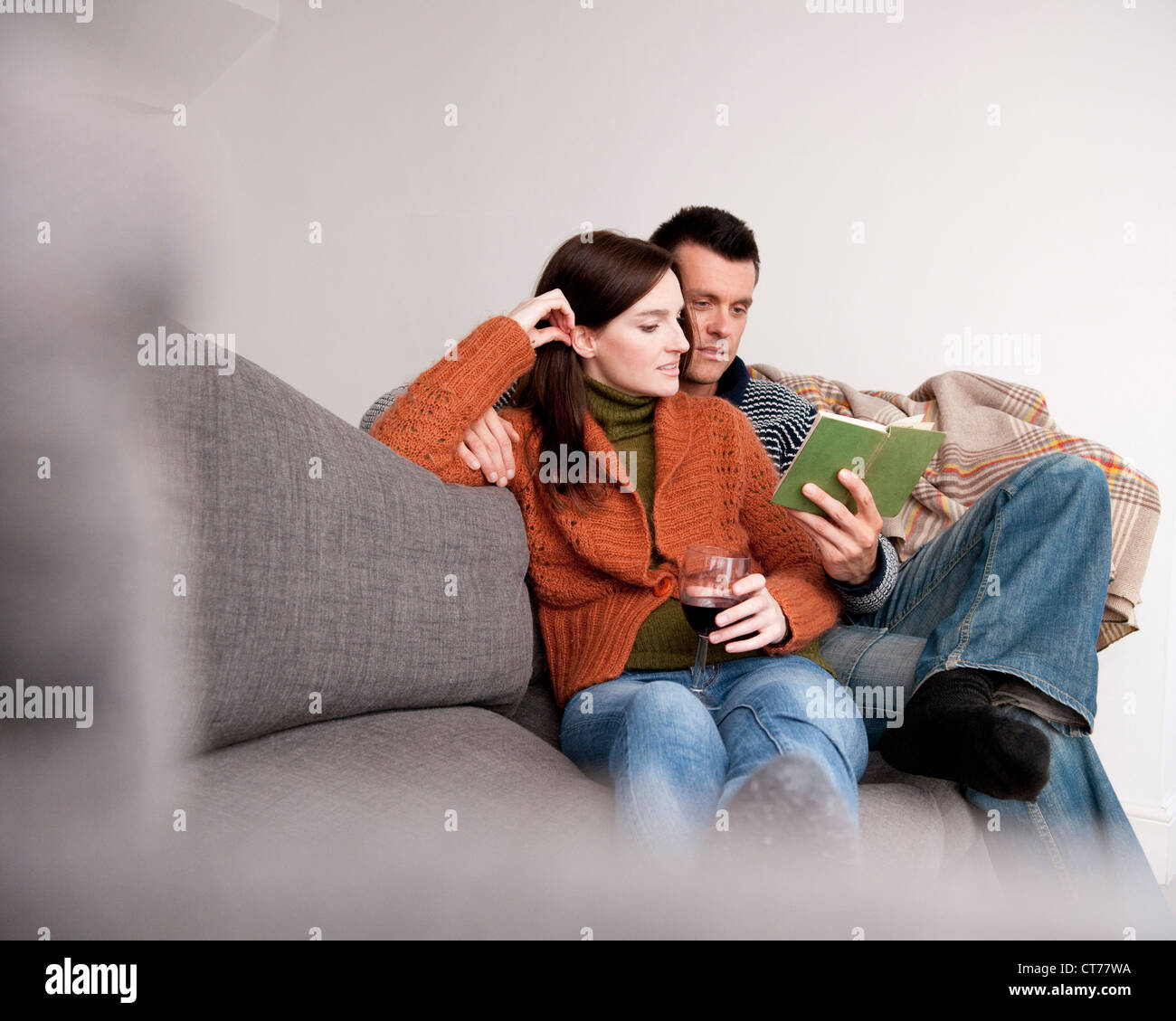 Young couple sitting on sofa reading book Banque D'Images