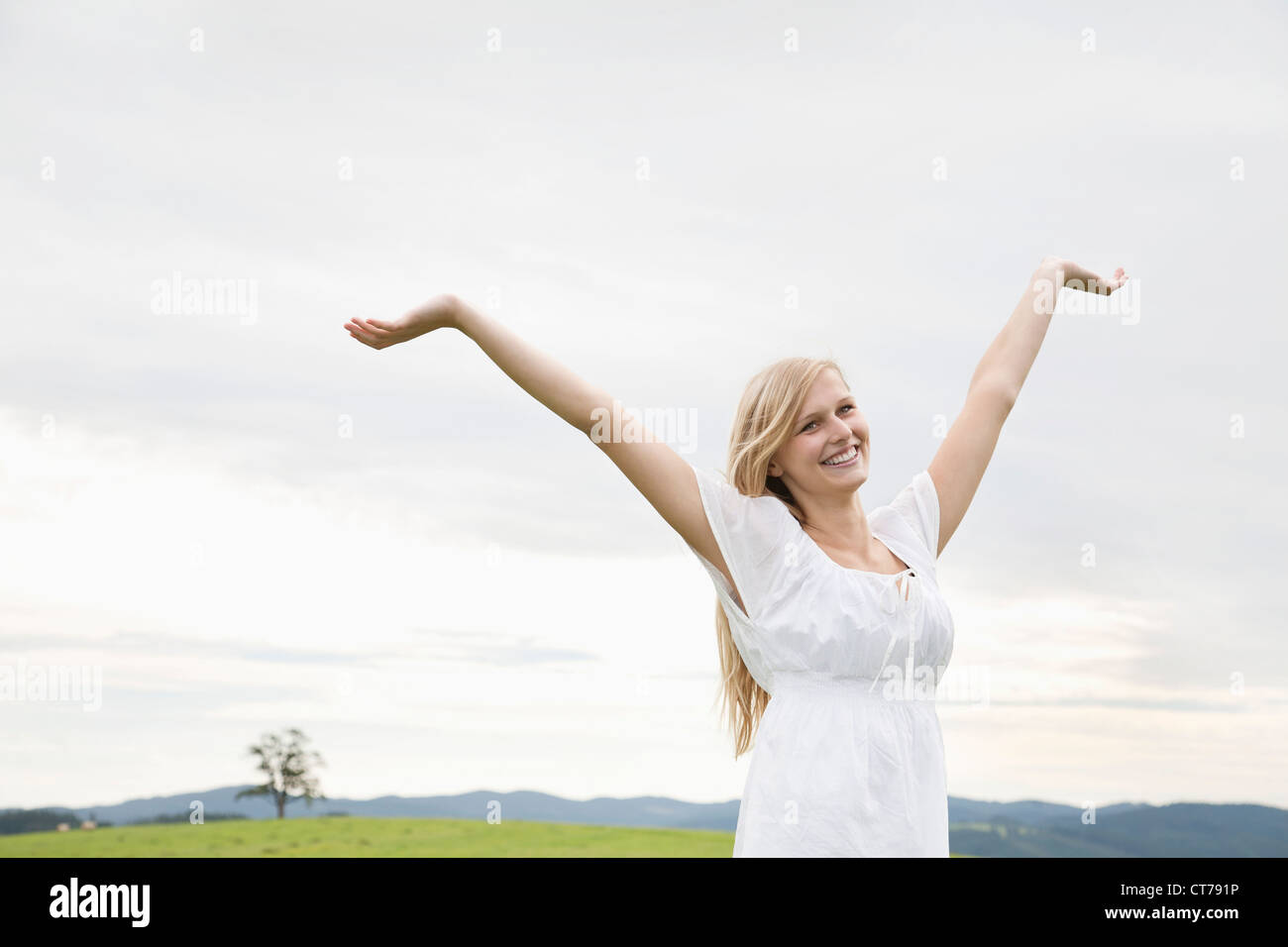 Jeune femme sur prairie d'élever ses bras en l'air Banque D'Images