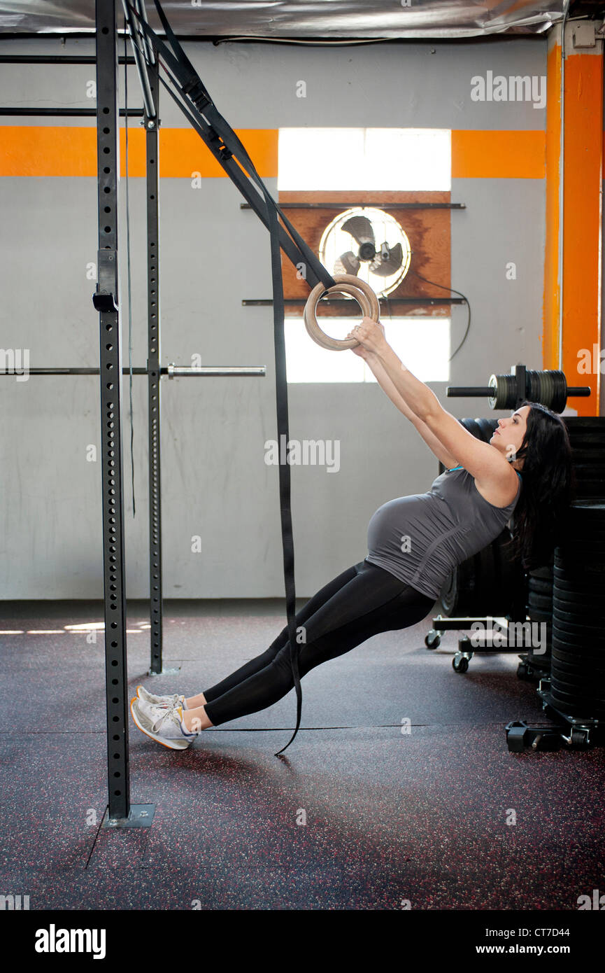 Jeune femme enceinte tirant les anneaux de gymnastique Banque D'Images