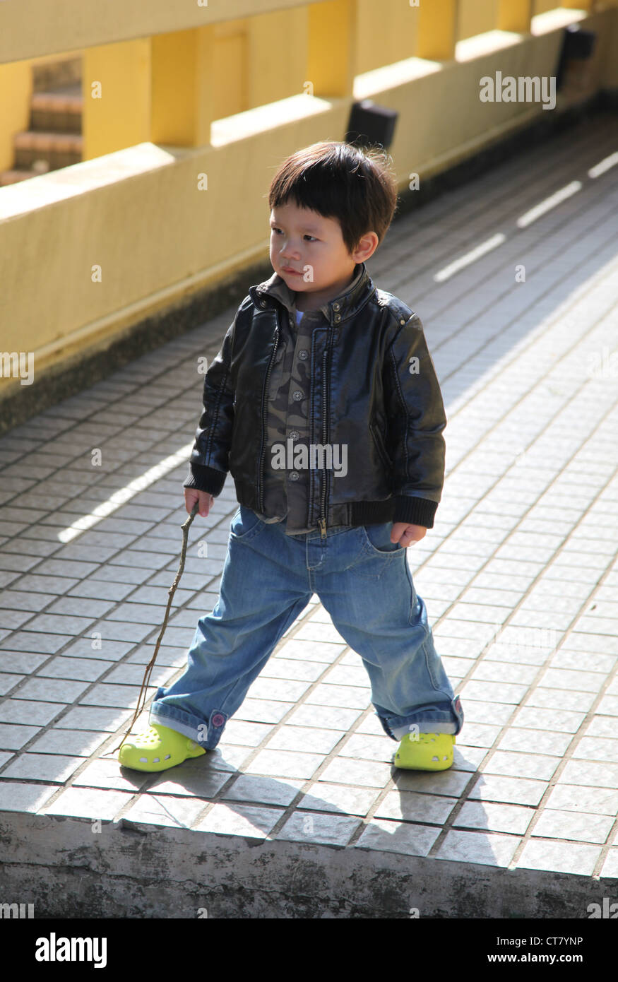 C'est une photo d'un petit garçon chinois qui agissent comme un agent de sécurité. Il est titulaire d'un bâton de bois comme arme et bloquer le chemin Banque D'Images