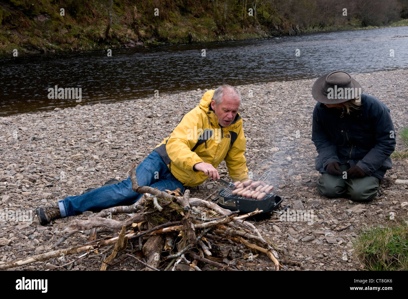 L'homme et la femme au barbecue saucisses à l'extérieur au bord de la rivière Banque D'Images