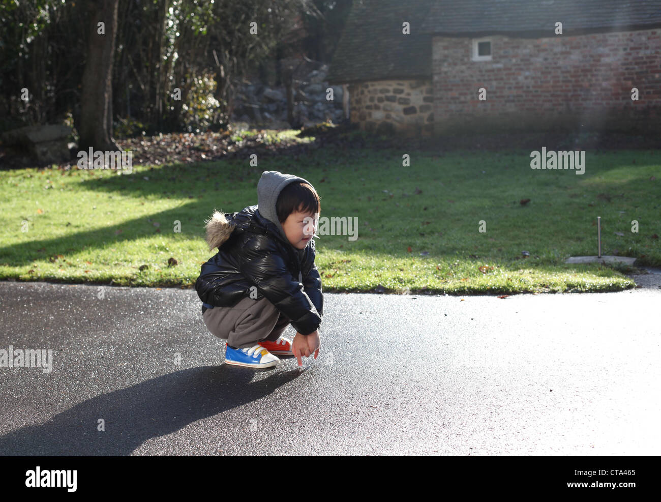 C'est une photo d'un petit garçon de 3 ans ou 4 ans qui est juste s'accroupir sur une route ou la cour dans une ferme de Normandie, France Banque D'Images
