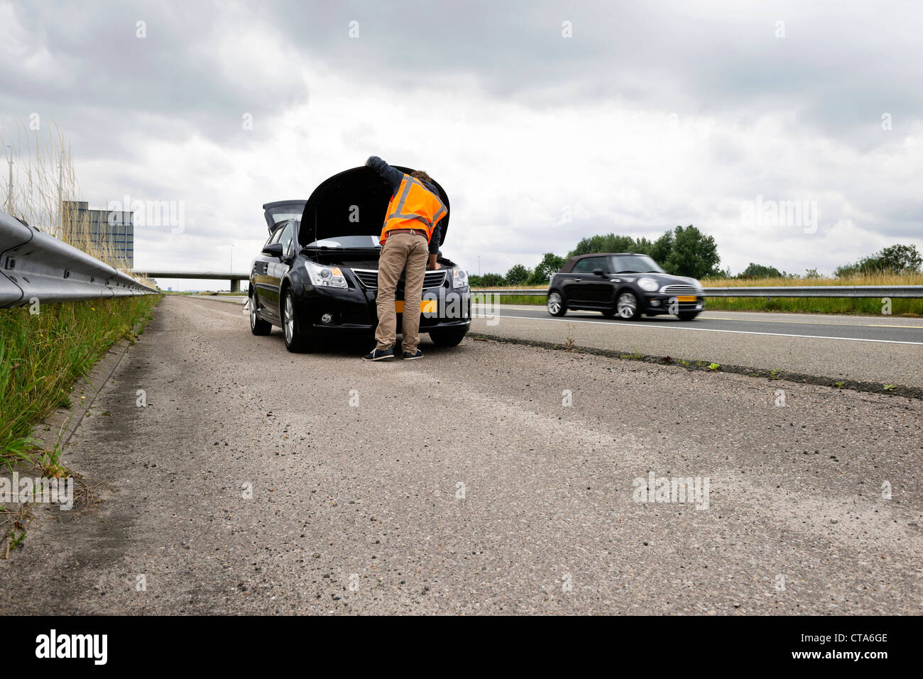 L'automobiliste en détresse, à essayer de réparer le moteur de sa voiture sur l'accotement d'une autoroute, avec le trafic passant par Banque D'Images