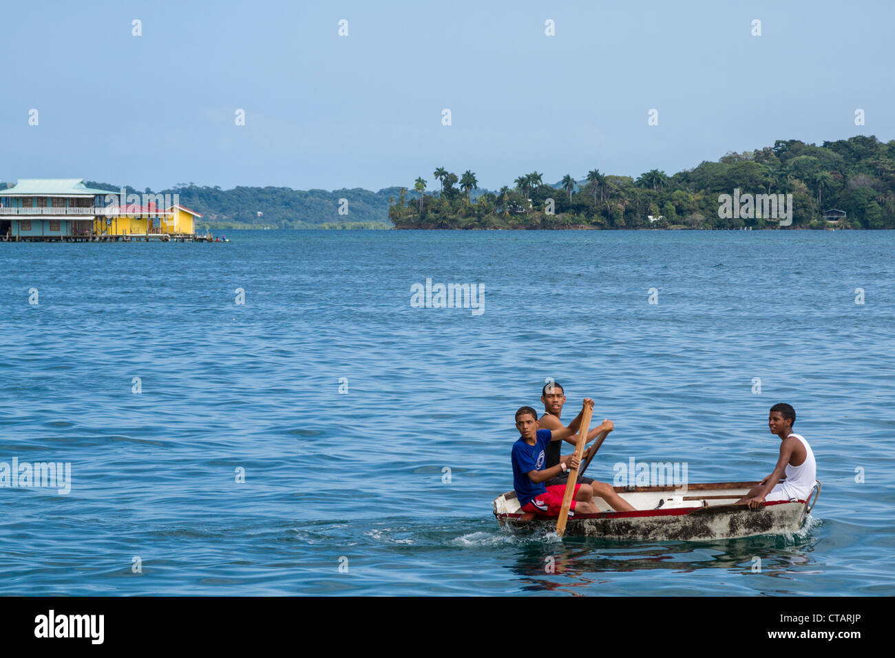 Trois garçons paddling un petit bateau entre l'Île de Colon et Isla Carenero, Bocas del Toro, PANAMA. Banque D'Images