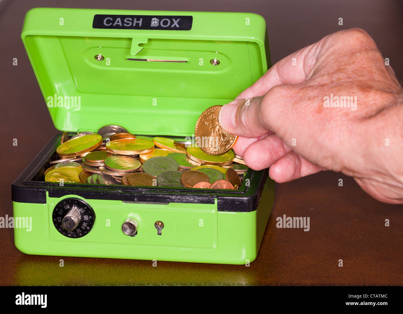 Caisse verte avec serrure à combinaison ouvrant sur des piles de pièces de monnaie dont l'or et l'argent Banque D'Images