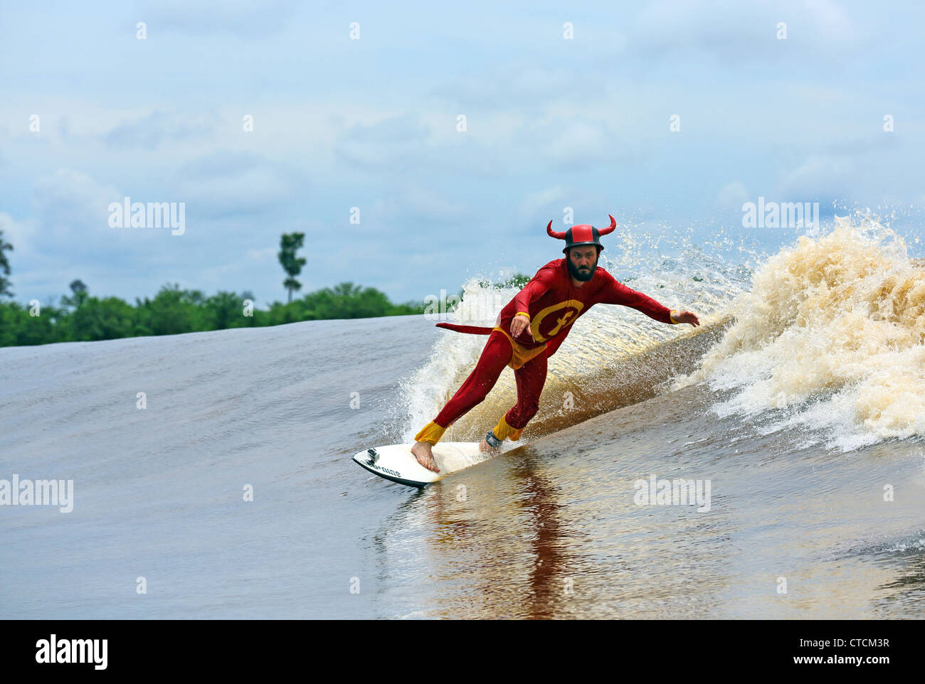 Homme étrange en costume de super-héro rouge river surf un mascaret vague sur la rivière Kampar, également connu sous le nom de Bono ou les 7 fantômes. Banque D'Images