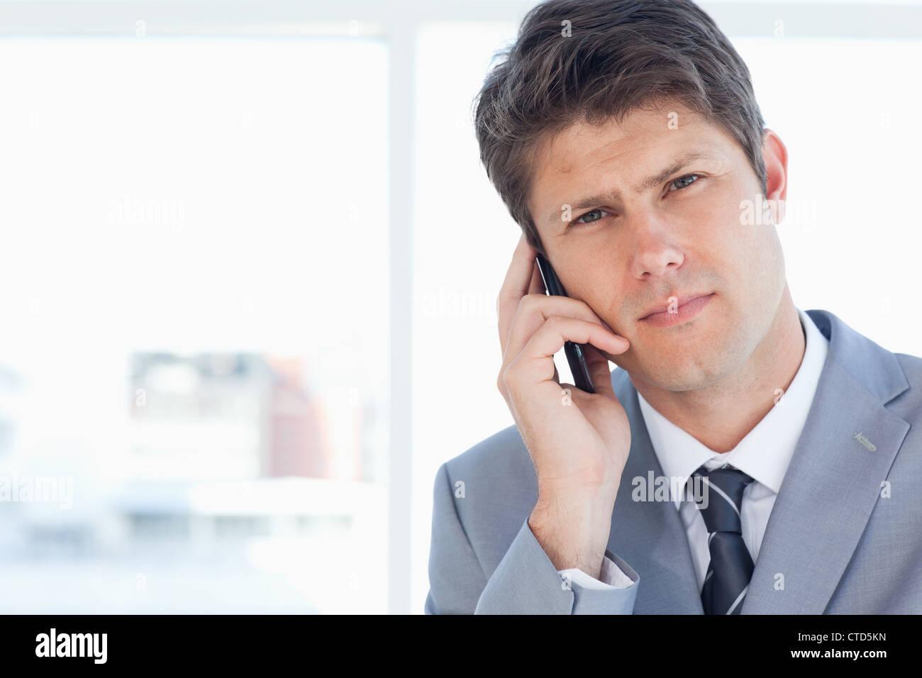Jeune cadre sérieusement parler au téléphone en face d'une fenêtre Banque D'Images