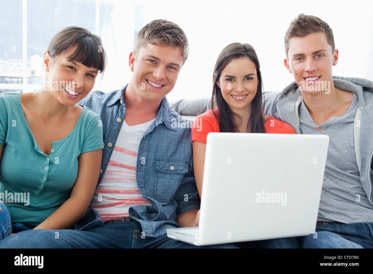 Un groupe d'amis assis avec un ordinateur portable comme ils regardent l'appareil photo Banque D'Images