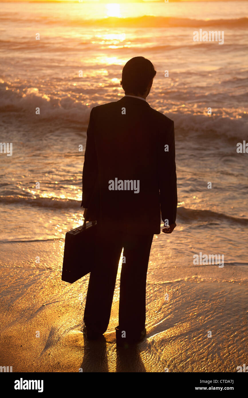 Jeune homme debout sur la plage au coucher du soleil Banque D'Images