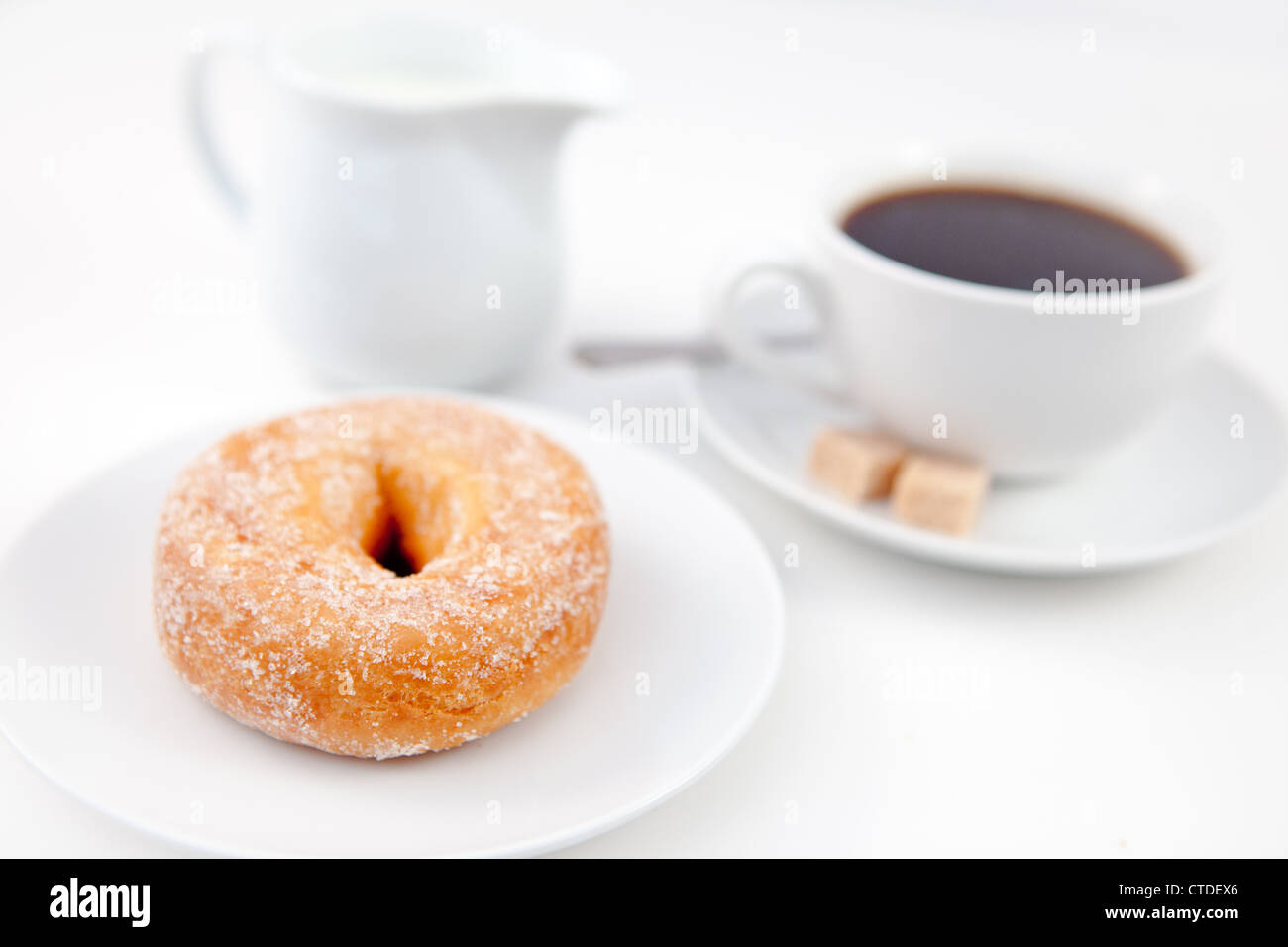 Donut de sucre glace et une tasse de café sur les plaques blanches avec le sucre et le lait Banque D'Images