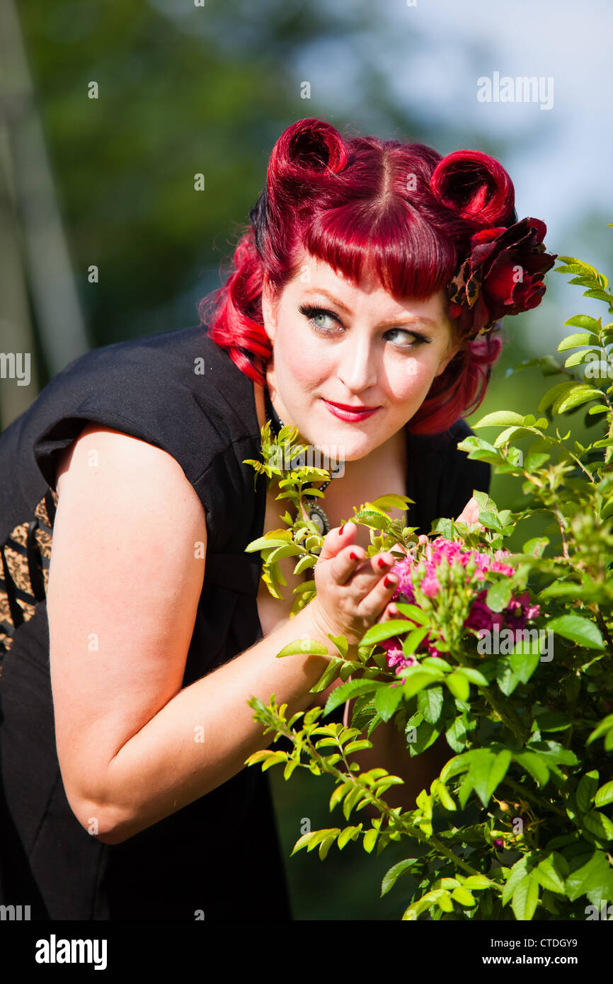 Style des années 1950 pinup model posing comme une épouse smelling flowers Banque D'Images