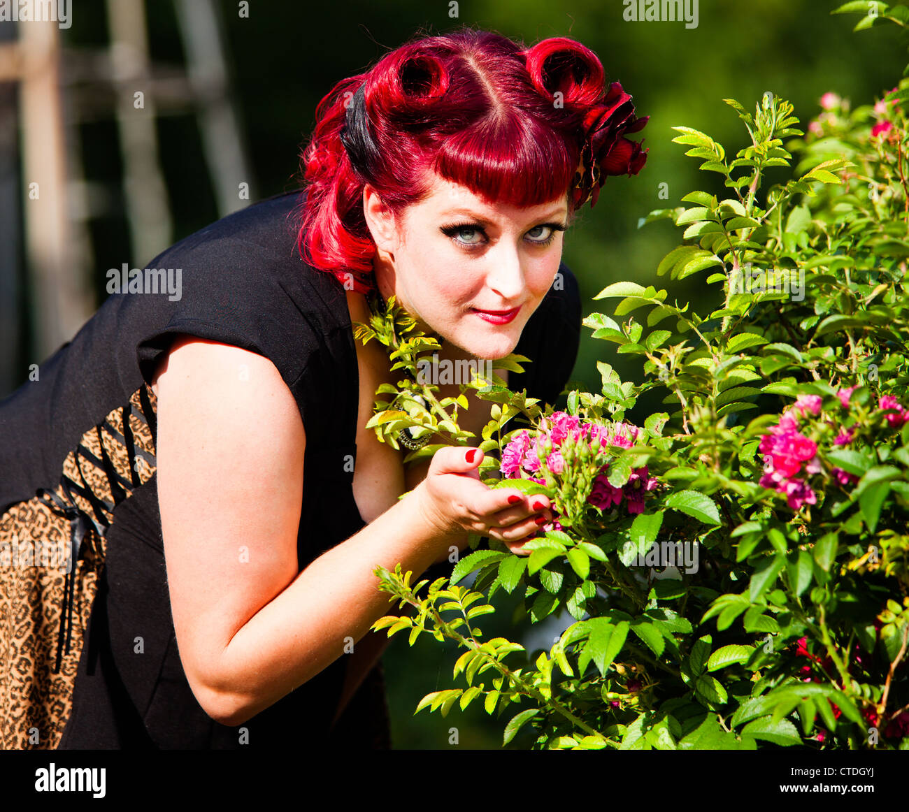 Style des années 1950 pinup model posing comme une épouse smelling flowers Banque D'Images