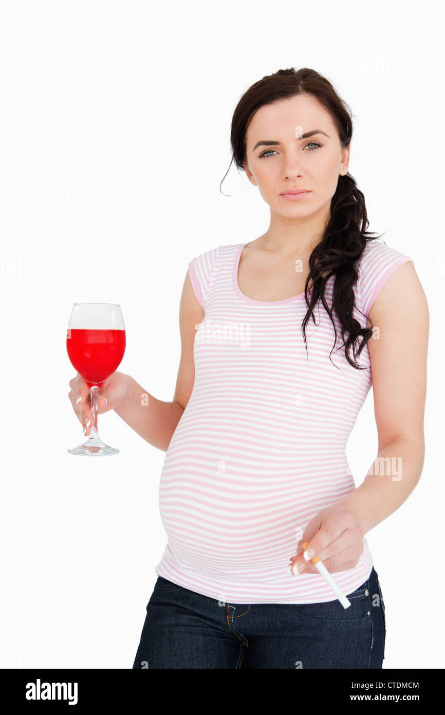 Jeune femme enceinte holding alcoholic drink and cigarette Banque D'Images