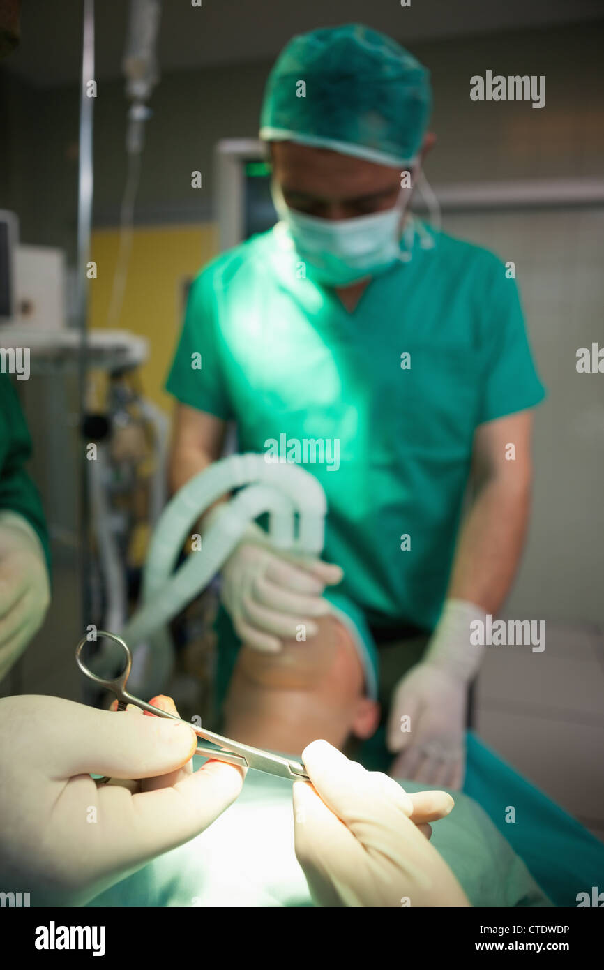 Ciseaux chirurgicaux dans les mains gantées sur un patient de couchage Banque D'Images