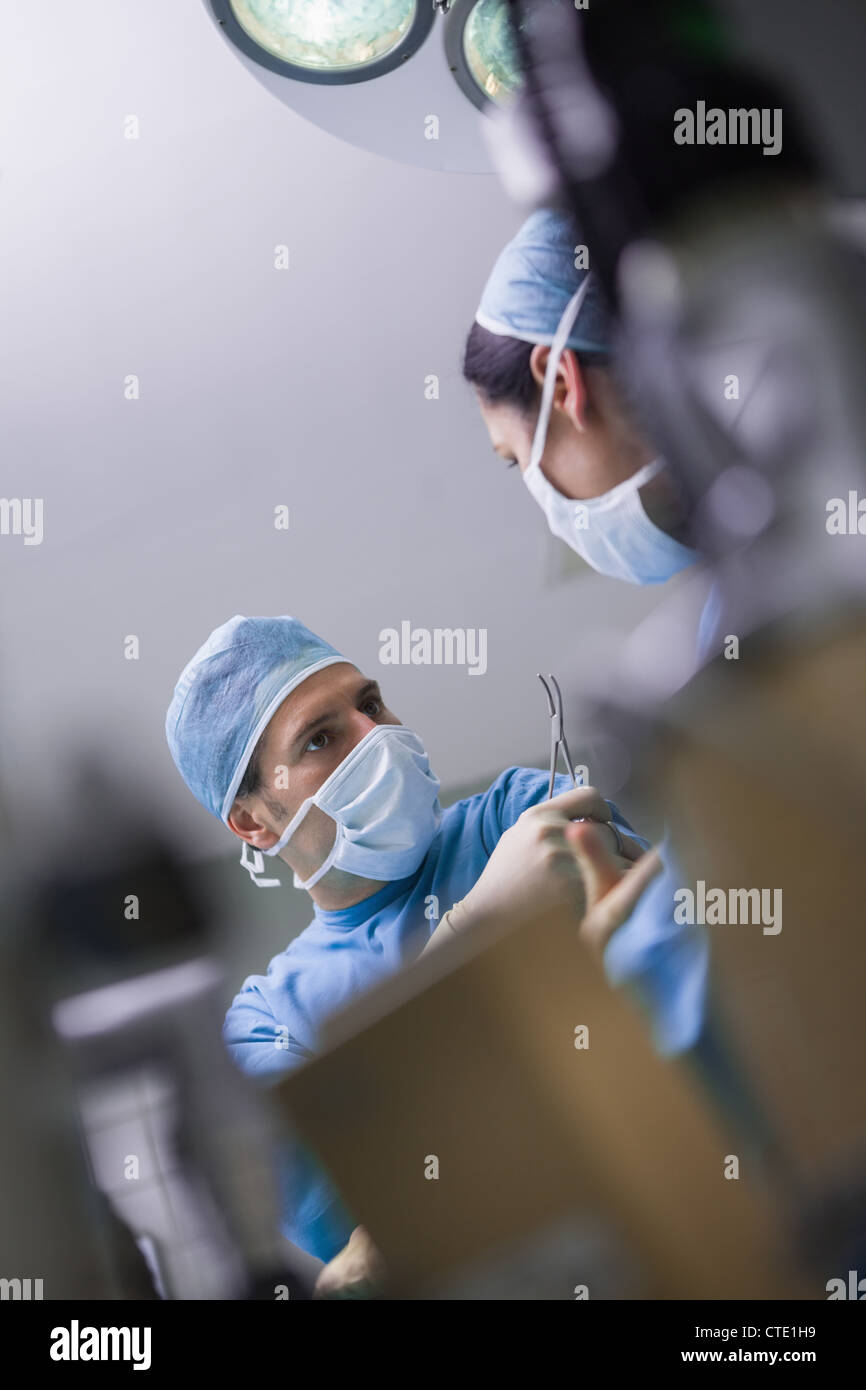 Médecin sérieux donnant un ciseaux chirurgicaux d'une infirmière Banque D'Images