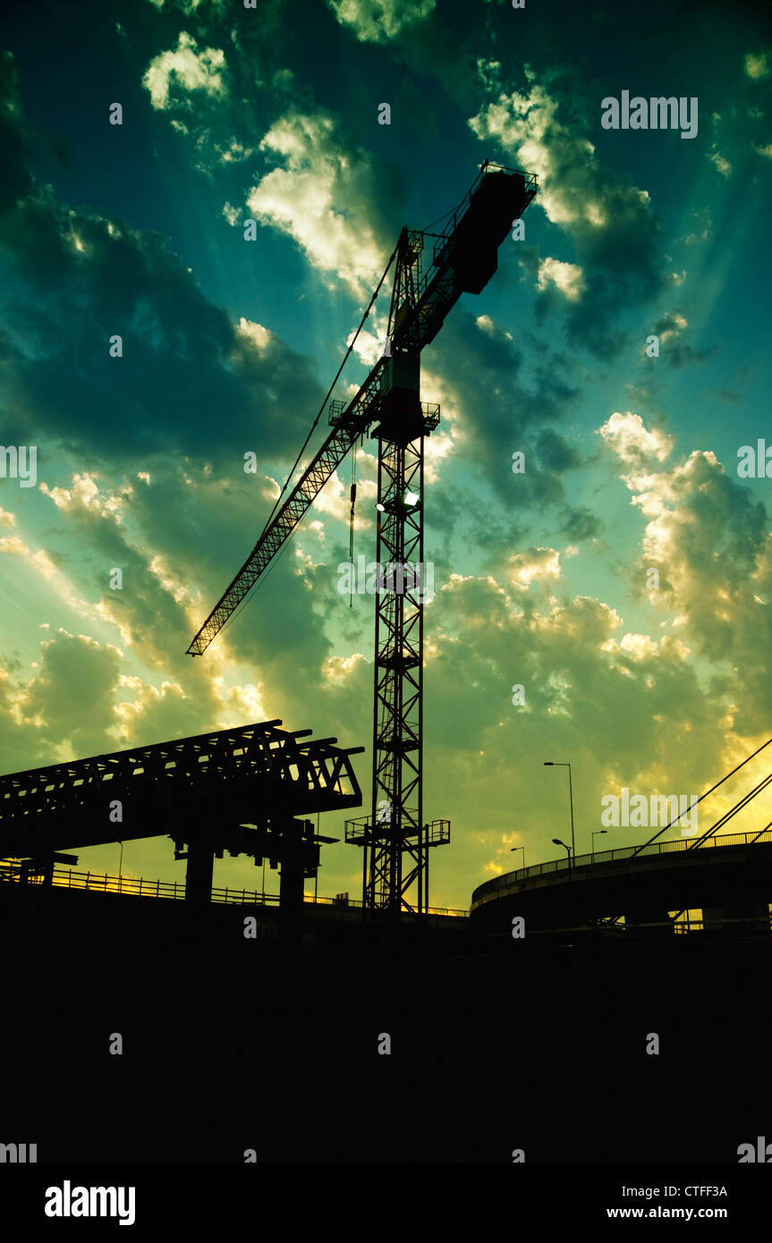Silhouettes de grues de construction et d'un pont dans le crépuscule contre le ciel coloré. Banque D'Images
