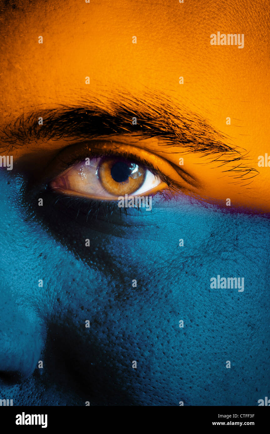 Pavillon bleu et orange sur le visage peint d'un partisan de l'équipe de sport, Close up d'un œil masculin. Banque D'Images