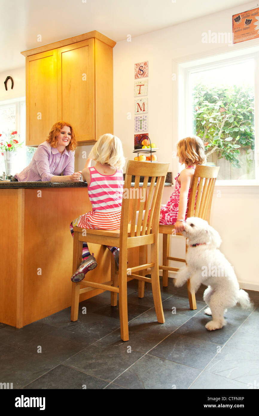 Une mère et ses deux filles sont dans la cuisine, une fille est de nourrir le chien. Banque D'Images