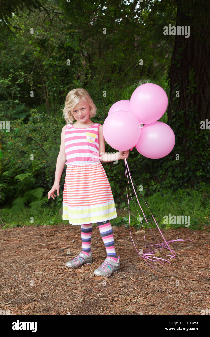 Une petite fille en robe rayée est holding ballons roses. Banque D'Images