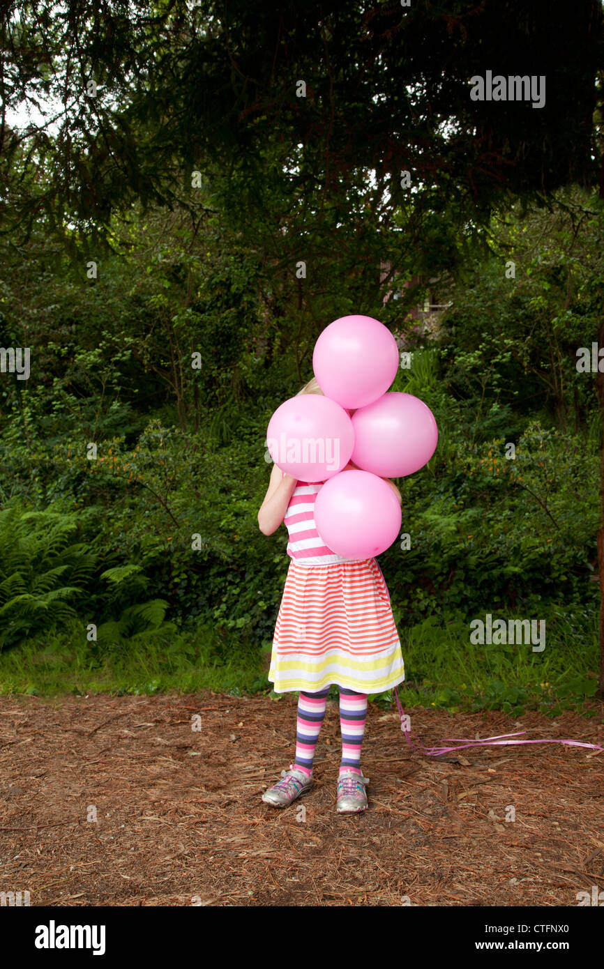 Une petite fille en robe rayée est holding ballons roses. Banque D'Images