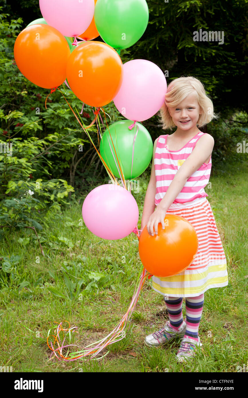 Petite fille blonde dans une robe rayée holding ballons colorés. Banque D'Images