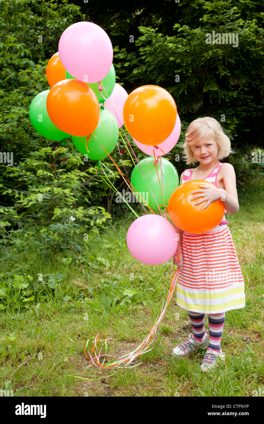 Petite fille blonde dans une robe rayée holding ballons colorés. Banque D'Images