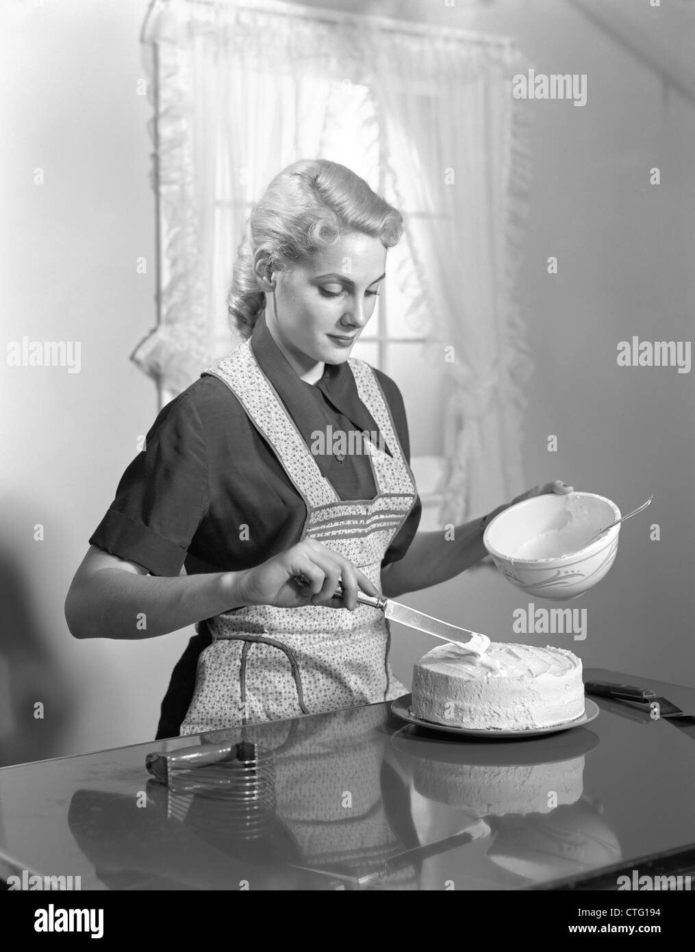 1940 FEMME EN PORTANT UN TABLIER CUISINE CAKE glaçage à la piscine Banque D'Images