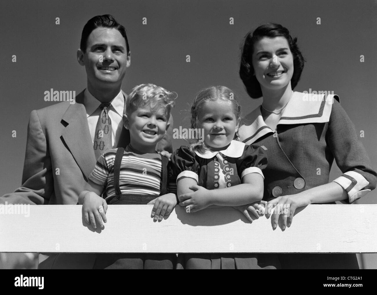 1950 PORTRAIT SMILING FAMILY Père Mère Fils Fille debout derrière une clôture blanche Banque D'Images