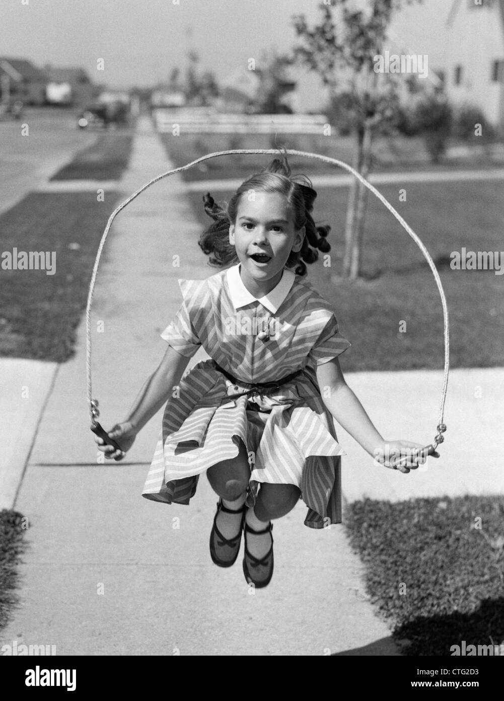 1950 GIRL JUMPING ROPE ON SIDEWALK Banque D'Images