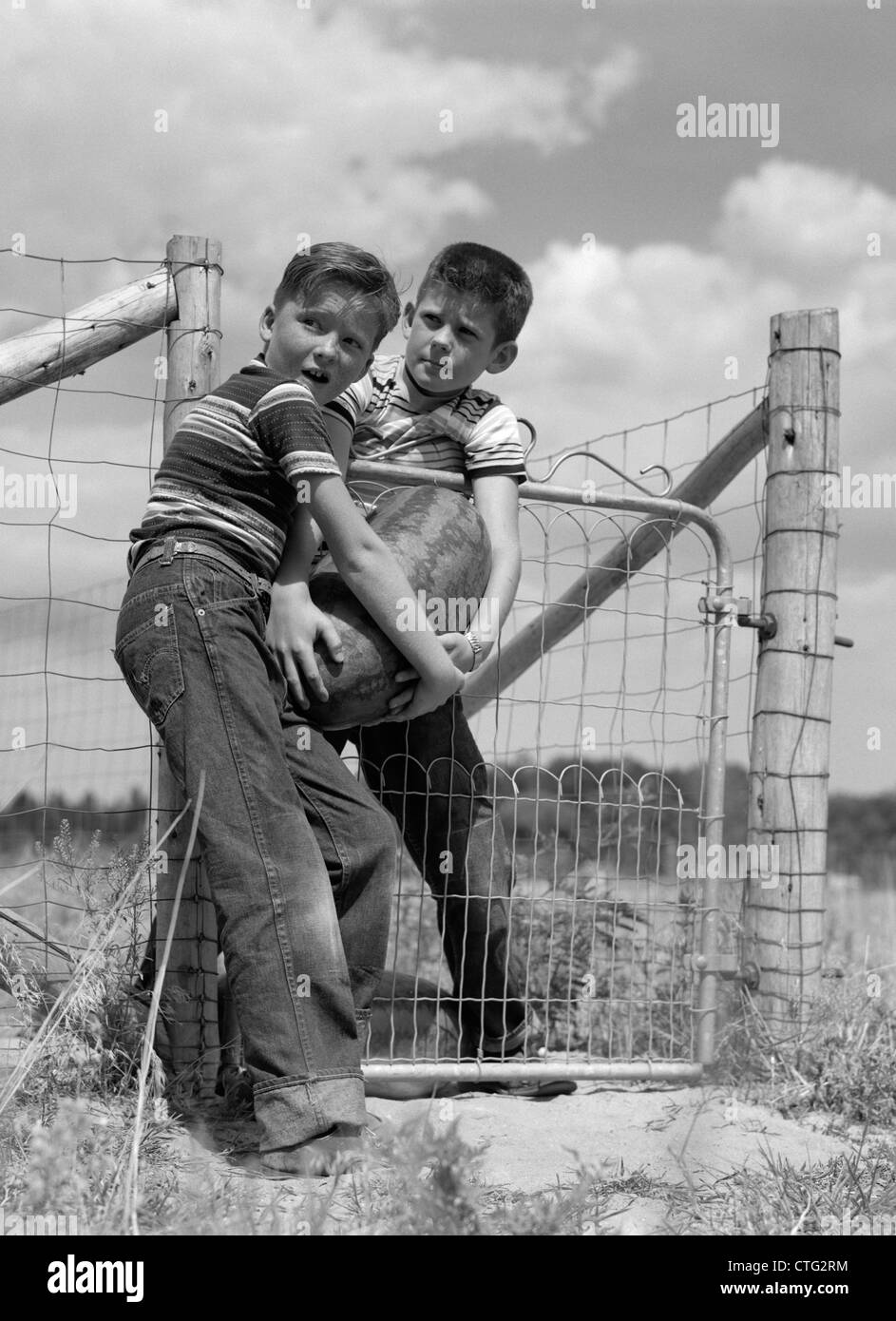 Des années 1970, deux garçons de ferme chez T-SHIRTS ET JEANS BLEU VOL GRANDE PASTÈQUE À PARTIR D'UN JARDIN Banque D'Images