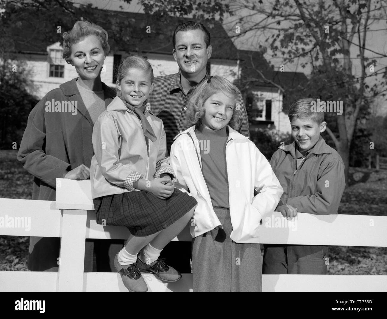 1960 PORTRAIT SMILING FAMILY PÈRE MÈRE DEUX FILLES FILS PAR CLÔTURE BLANCHE EN FACE DE LA MAISON DE BANLIEUE À L'AUTOMNE Banque D'Images