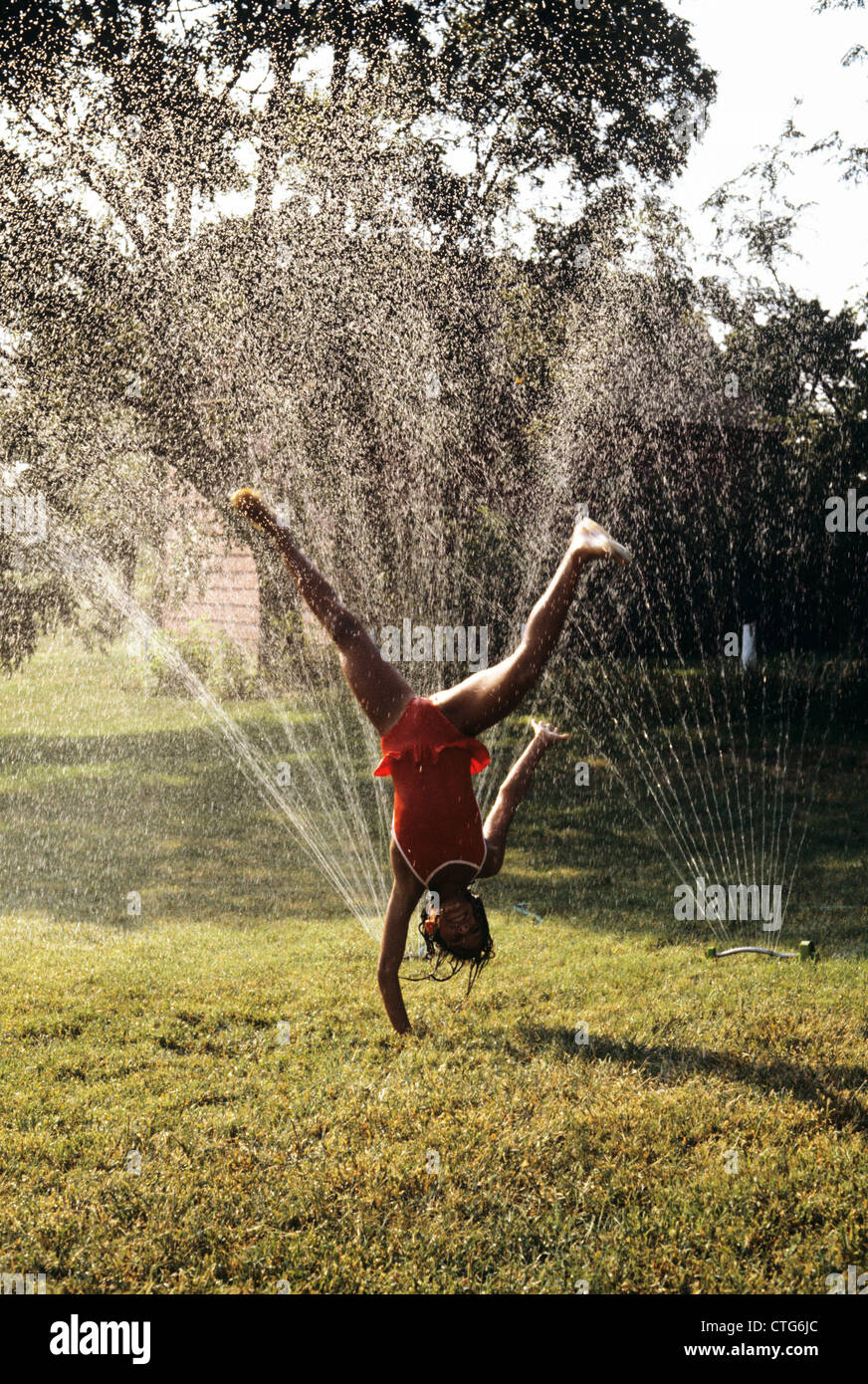 LITTLE GIRL CARTWHEELING PAR SPRINKLEUR PELOUSE Banque D'Images