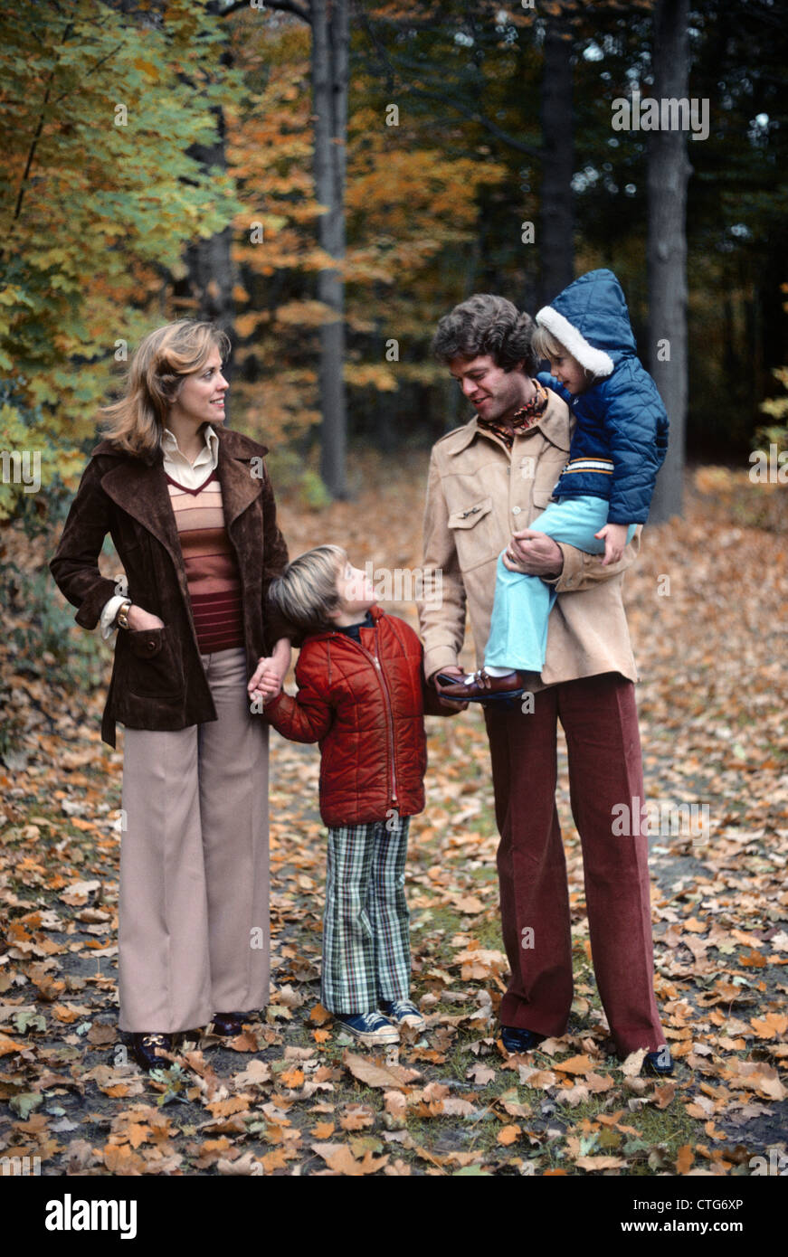 1970 FAMILLE DE QUATRE MARCHE DANS PAYSAGE D'AUTOMNE HOLDING HANDS FATHER CARRYING GIRL TALKING TO BOY Banque D'Images