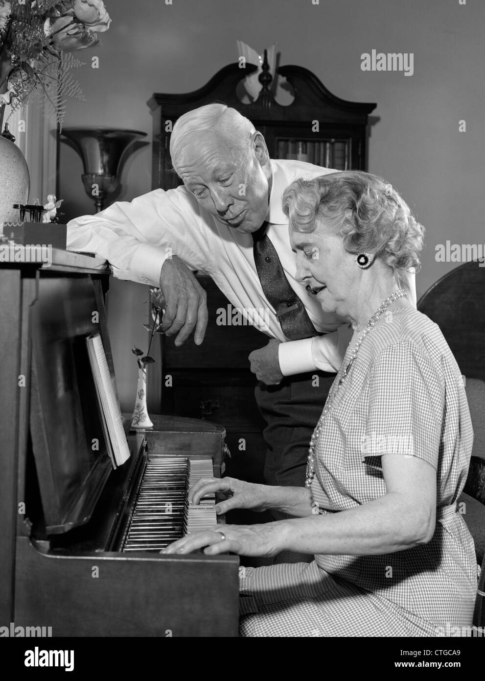 1960 femme âgée À JOUER DU PIANO AVEC SON MARI debout à côté de son chant Banque D'Images