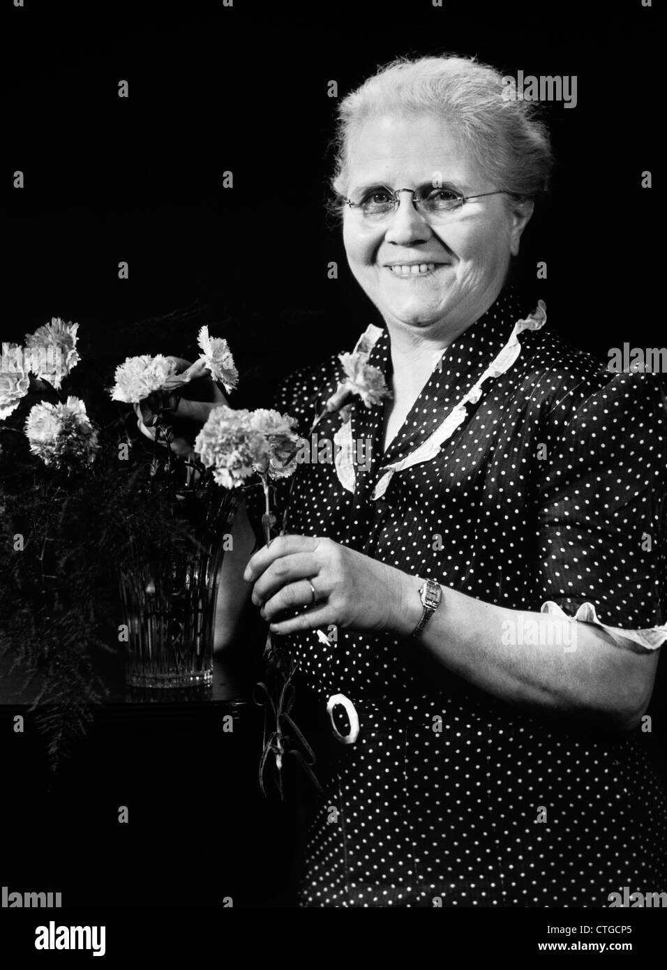 1940 femme âgée de mettre dans un vase de fleurs d'OEILLET LOOKING AT CAMERA Banque D'Images