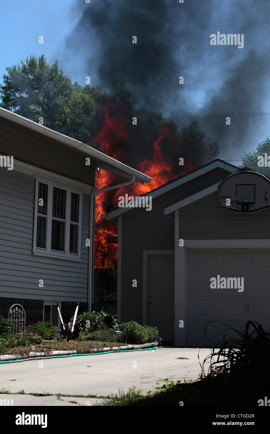 Un feu brûle derrière une maison et garage. Banque D'Images