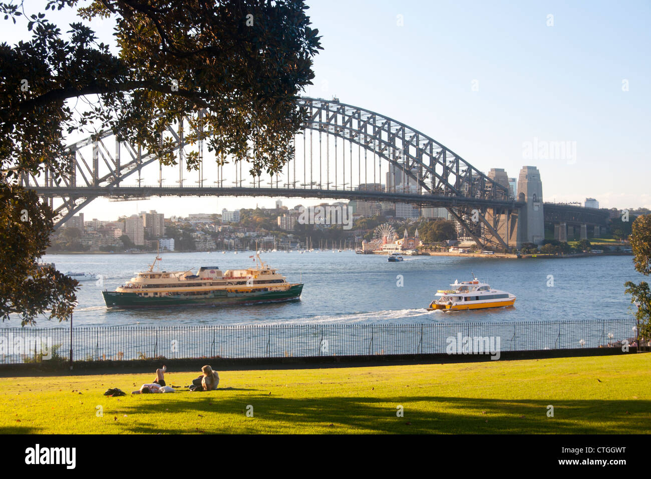 Deux femmes se trouvant dans la région de Park au coucher du soleil avec Bateau et Ferry Manly passant et Sydney Harbour Bridge en arrière-plan Sydney NSW Australie Banque D'Images