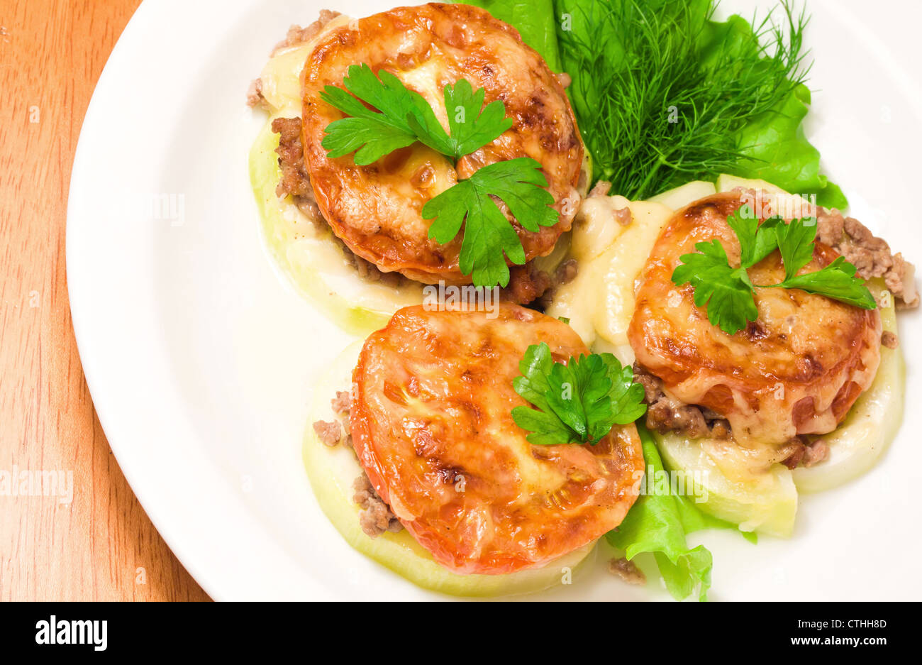 Soutenu vegetable marrow farcies de viande, de tomates, fromage et verts sur une plaque blanche Banque D'Images