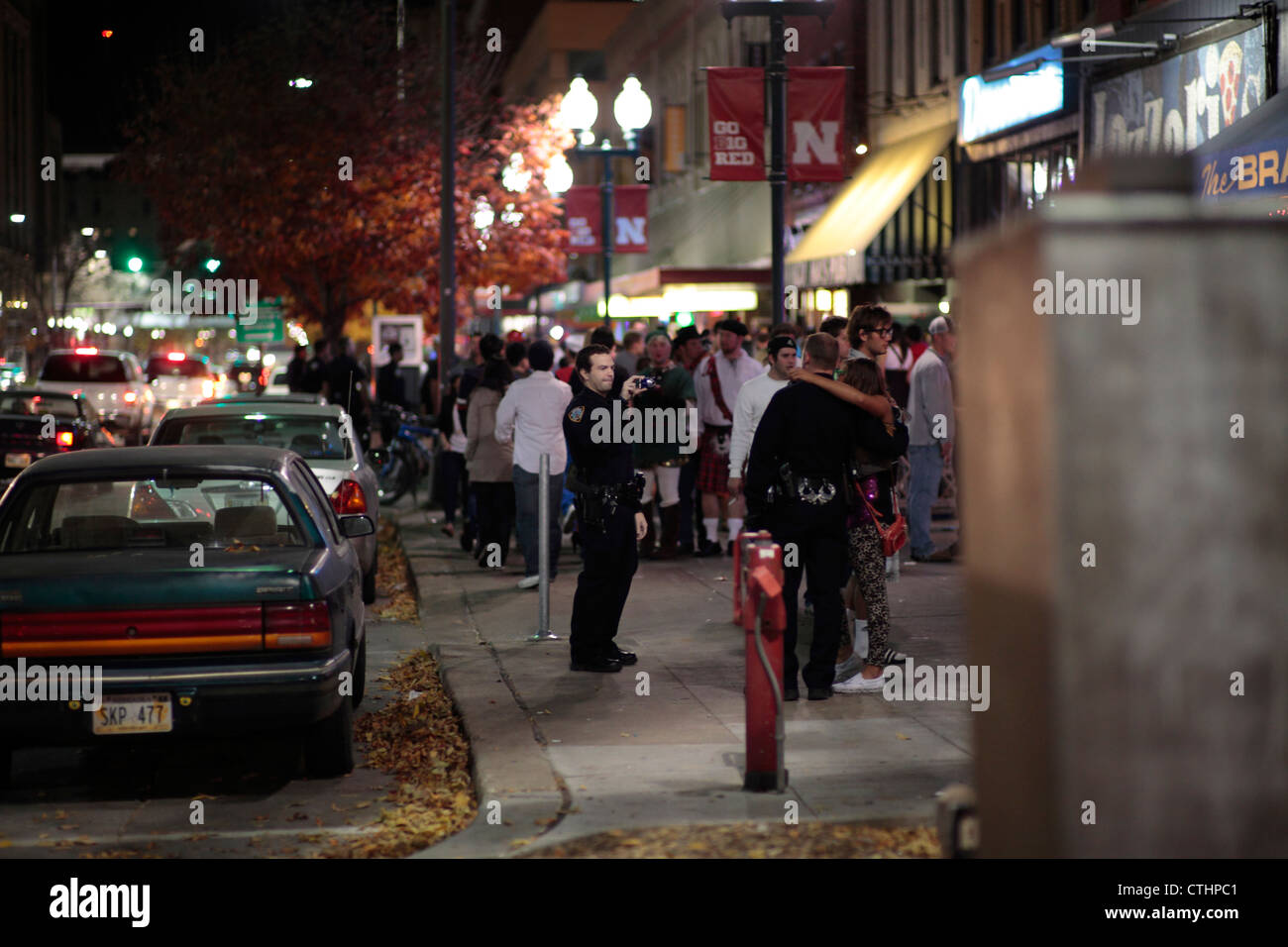 Un agent de police prend une photo de fêtards Halloween avec son partenaire, le soir de l'Halloween sur un trottoir du centre-ville animé. Banque D'Images