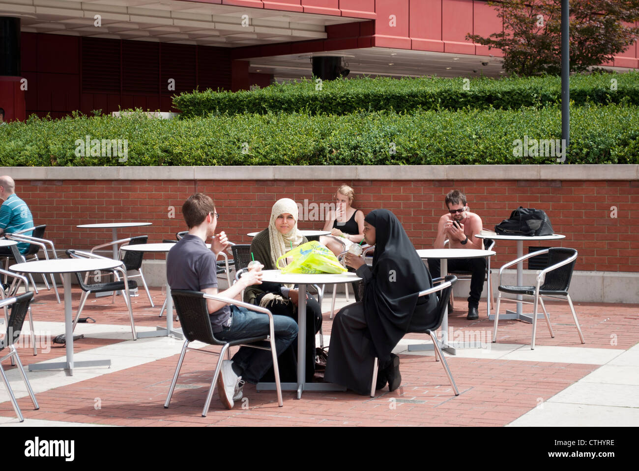Les gens assis à des tables à l'extérieur de la British Library dont deux femmes musulmanes Banque D'Images