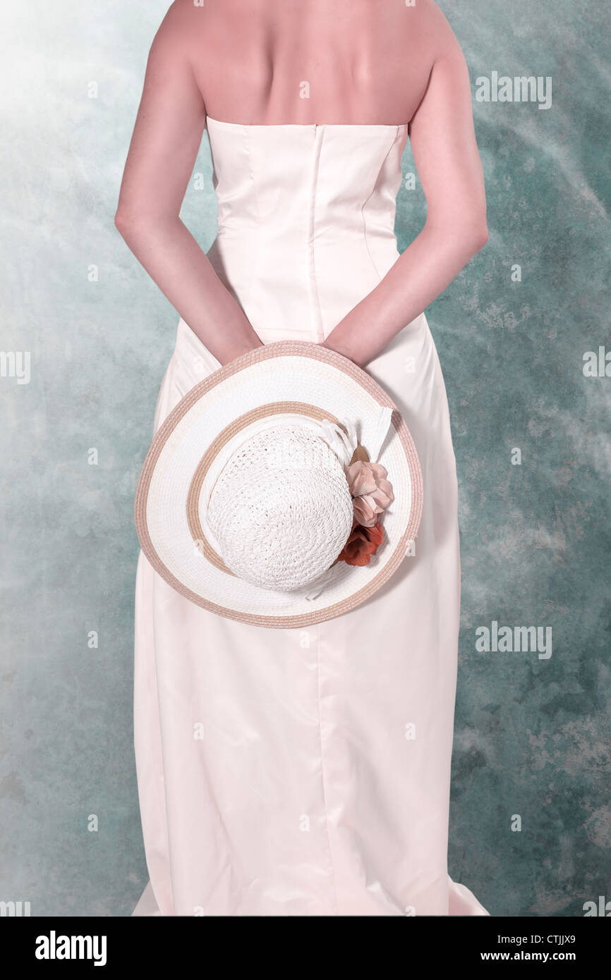 Une femme en robe blanche tenant un chapeau de paille derrière son dos Banque D'Images