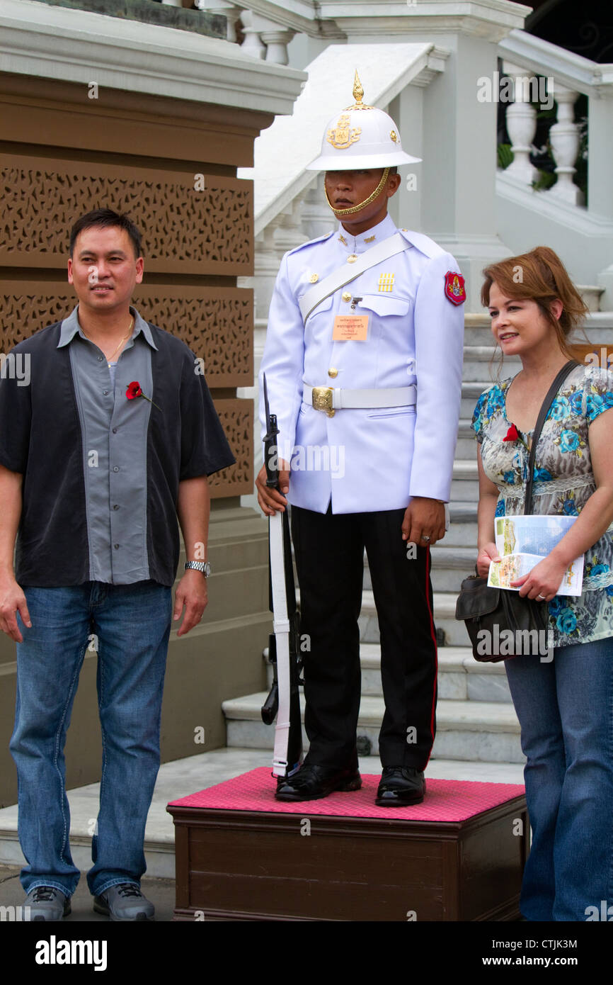 Des touristes posent pour une photo avec un garde portant un uniforme blanc au Grand Palais à Bangkok, Thaïlande. Banque D'Images