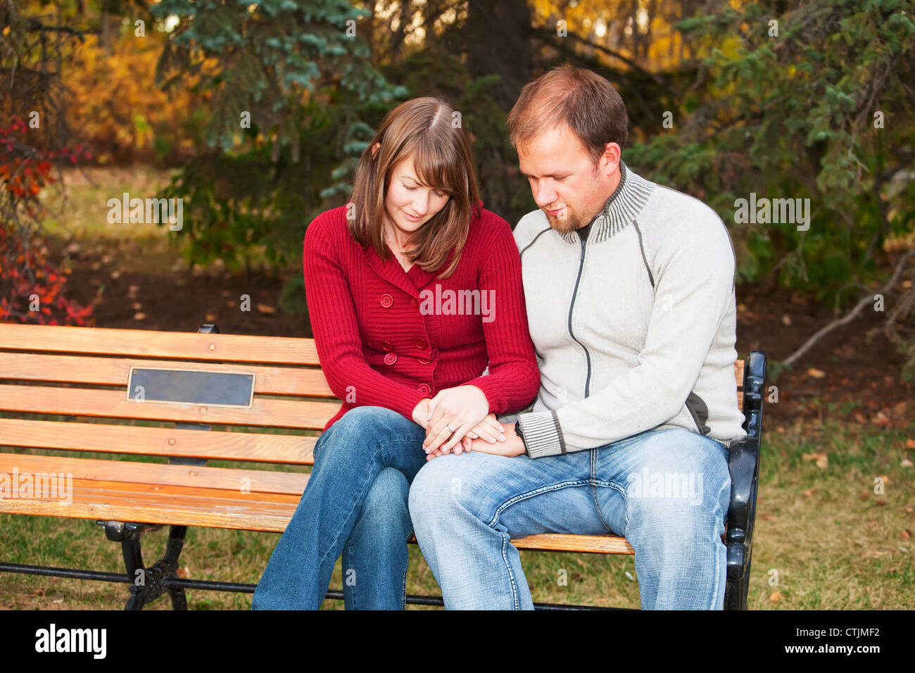 Deux jeunes mariés priant ensemble sur un banc de parc ; Edmonton, Alberta, Canada Banque D'Images