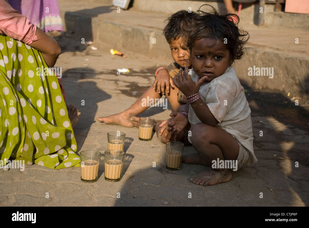 Coincé de la pauvreté des enfants assis sur le trottoir avec verres à thé dans l'avant-plan - Mumbai, Inde Banque D'Images