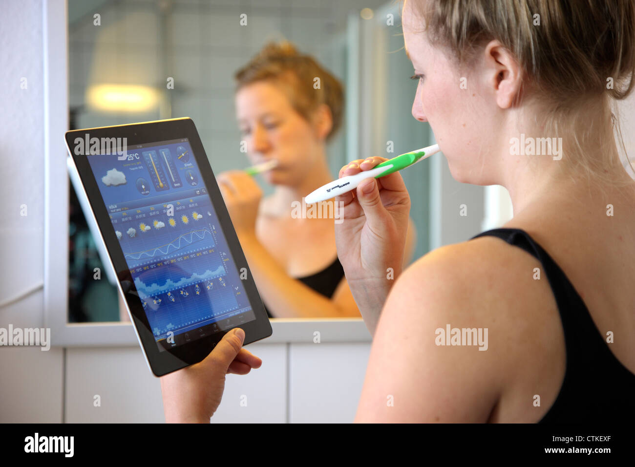 Jeune femme se brosser les dents dans la salle de bains. En utilisant un IPad, tablet computer, la lecture des nouvelles, de la météo. Banque D'Images