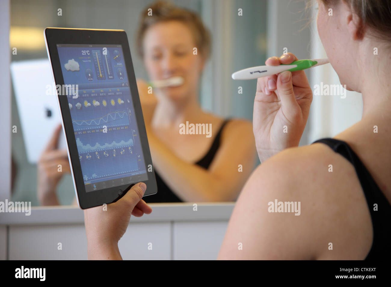 Jeune femme se brosser les dents dans la salle de bains. En utilisant un IPad, tablet computer, la lecture des nouvelles, de la météo. Banque D'Images