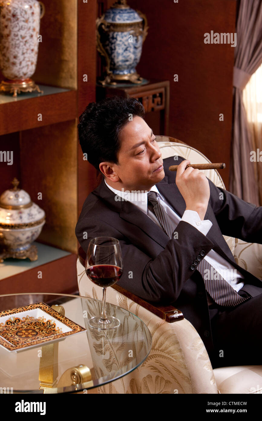 Mature businessman profitant de cigare et de vin dans une chambre de luxe Banque D'Images