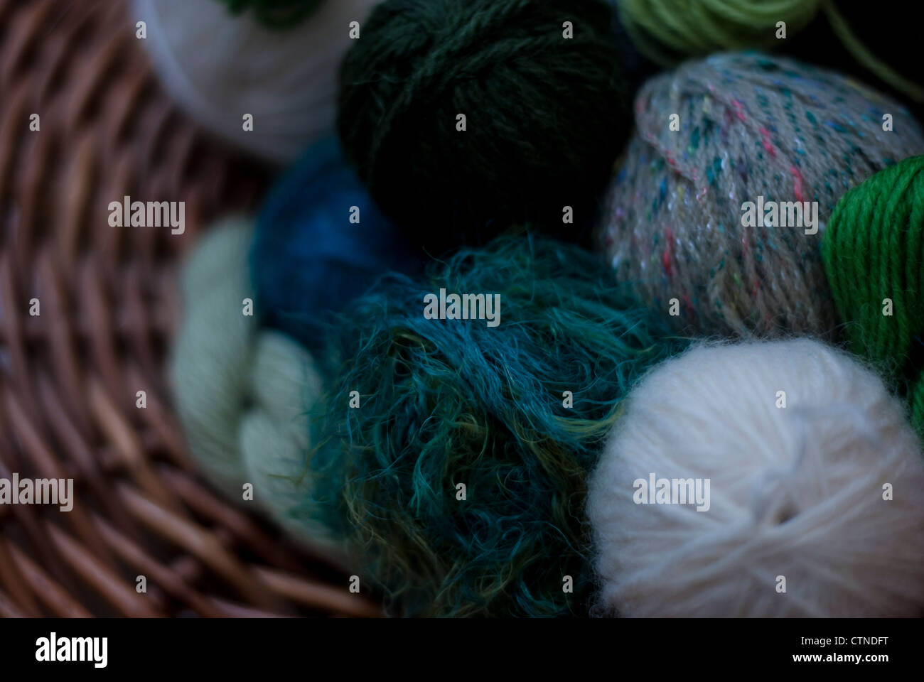 Close up de balles de laine dans les tons de vert, blanc et beige dans un panier tressé. Banque D'Images