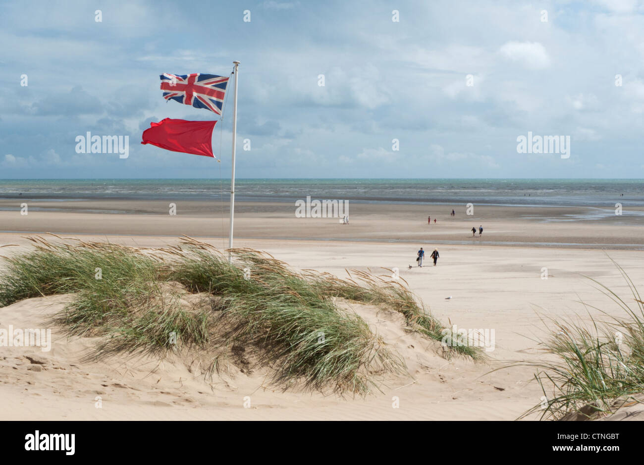 Union jack flag et red flag flying des dunes sur la plage par un jour de vent à marée basse Banque D'Images